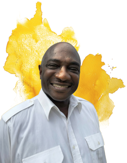 A smiling Black man wearing a white button-up shirt stands against a yellow painted background, conveying warmth, approachability, and confidence.